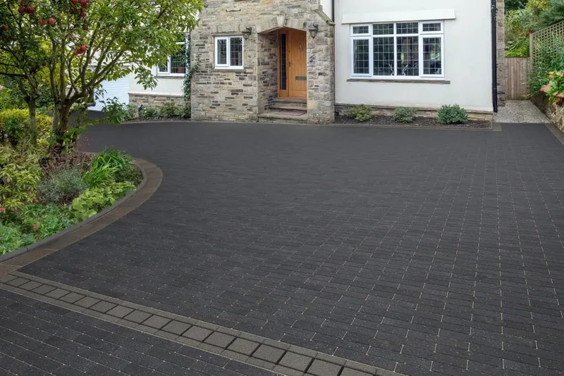 A block-paved driveway with a curved edge in front of a stone-fronted house